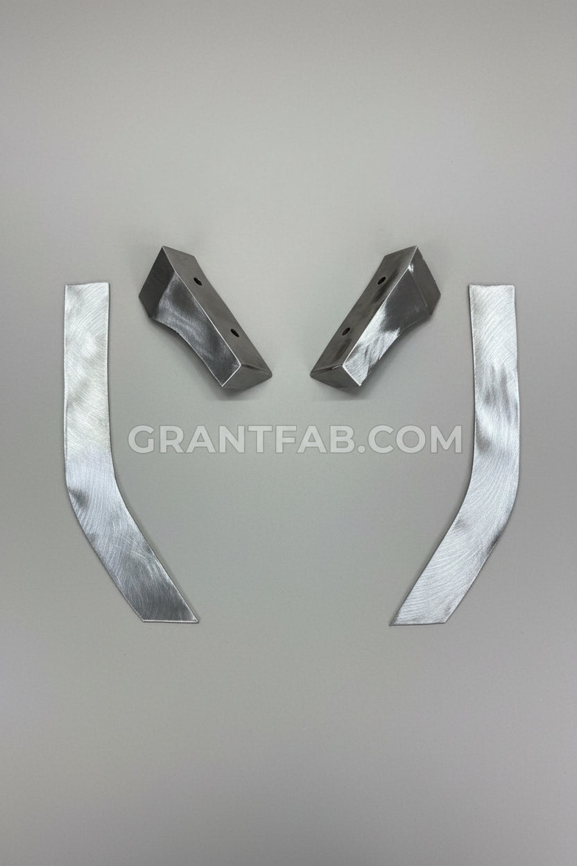 Four machined metal parts, including two angled bracket-like pieces and two curved flat strips, arranged on a brown cardboard background.